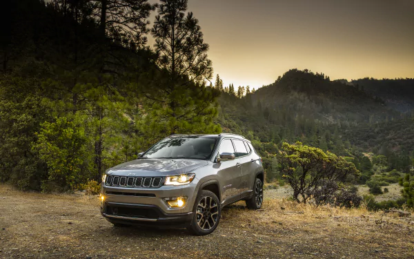 Silver Jeep Compass SUV car parked on a dirt overlook with forested hills at dusk — 2K Quad HD PC desktop wallpaper/background.