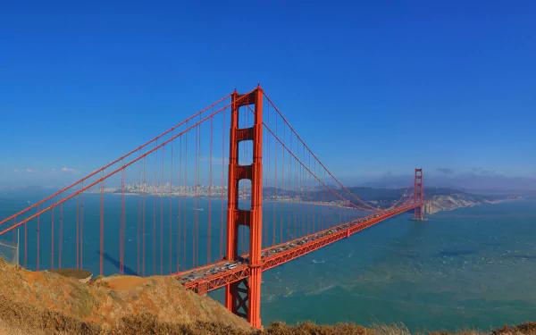 8K Ultra HD desktop wallpaper of the man-made Golden Gate Bridge spanning San Francisco Bay under a clear blue sky.