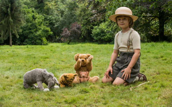 HD wallpaper of a person posing as Christopher Robin with plush toys in a grassy field.
