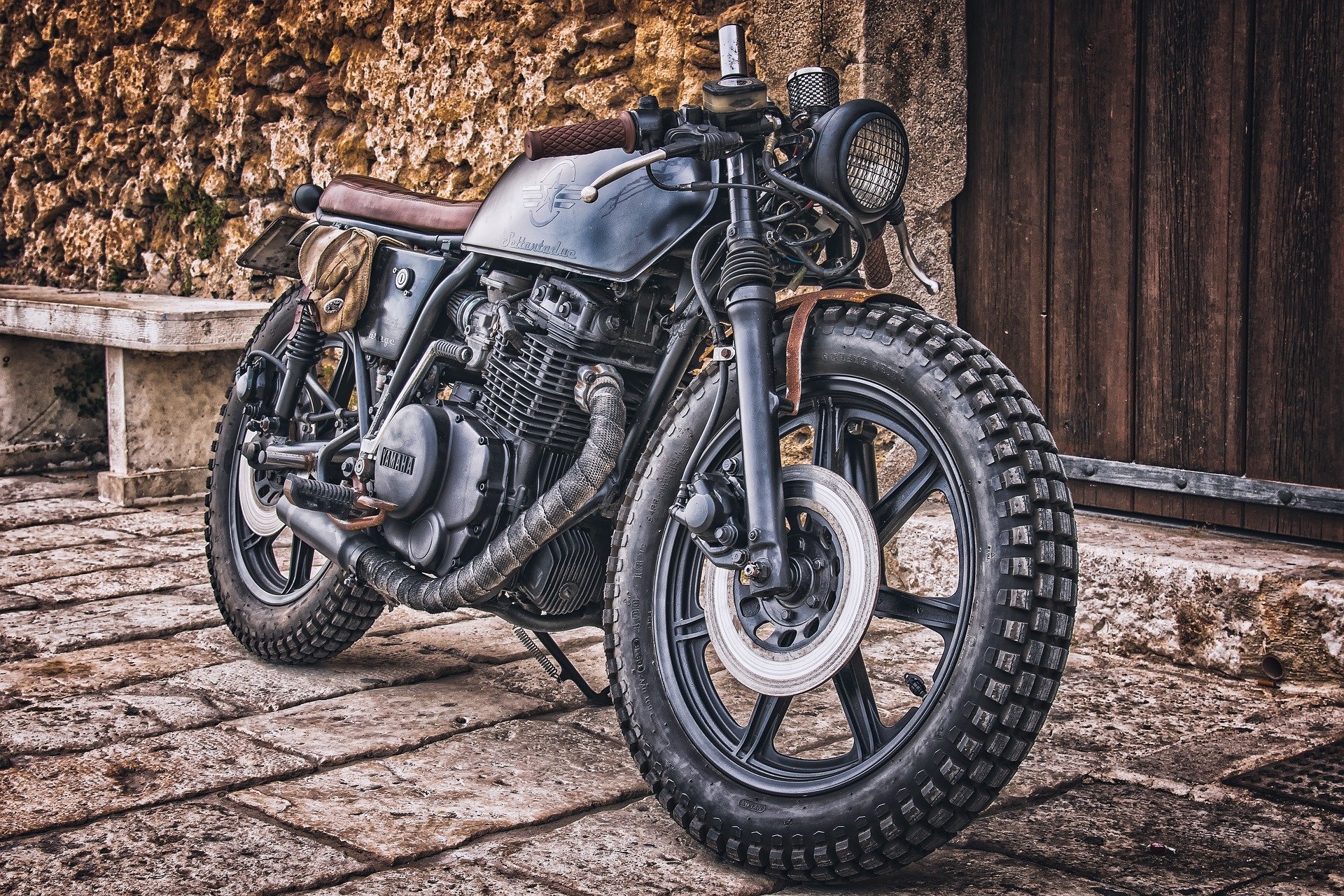 HDR HD PC desktop wallpaper and background: Yamaha motorcycle vehicle — a vintage cafe‑racer parked on cobblestones against a rustic stone wall and wooden door.
