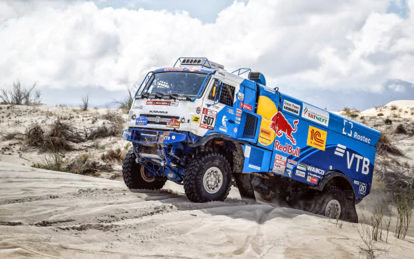 A Red Bull Kamaz rally truck races through sandy desert terrain under a cloudy sky, captured in 4K Ultra HD for a dynamic PC desktop wallpaper.