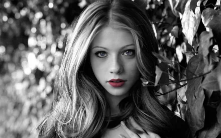 Black and white HD desktop wallpaper of celebrity Michelle Trachtenberg with striking blue eyes and red lips, surrounded by foliage.