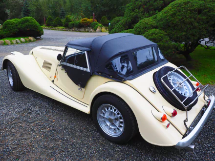 A vintage Morgan Plus 8 roadster with a soft top, parked on a gravel driveway surrounded by greenery, captured in 4K Ultra HD for a PC desktop wallpaper.