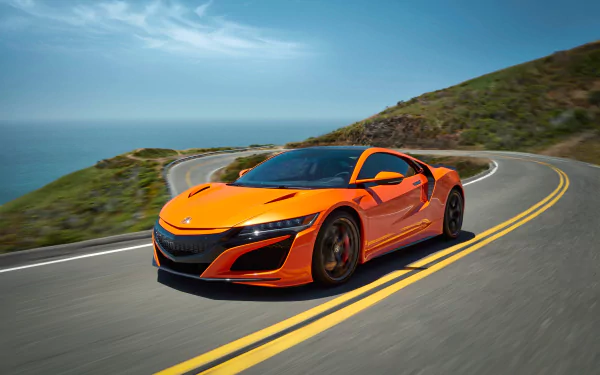 Orange Acura NSX supercar speeds along a winding coastal road under a clear blue sky, captured in stunning 4K Ultra HD for a vibrant desktop wallpaper.