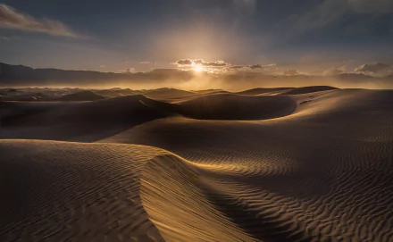 A stunning HD desktop wallpaper featuring a tranquil desert landscape with rippling sand dunes under a dramatic sunset sky.