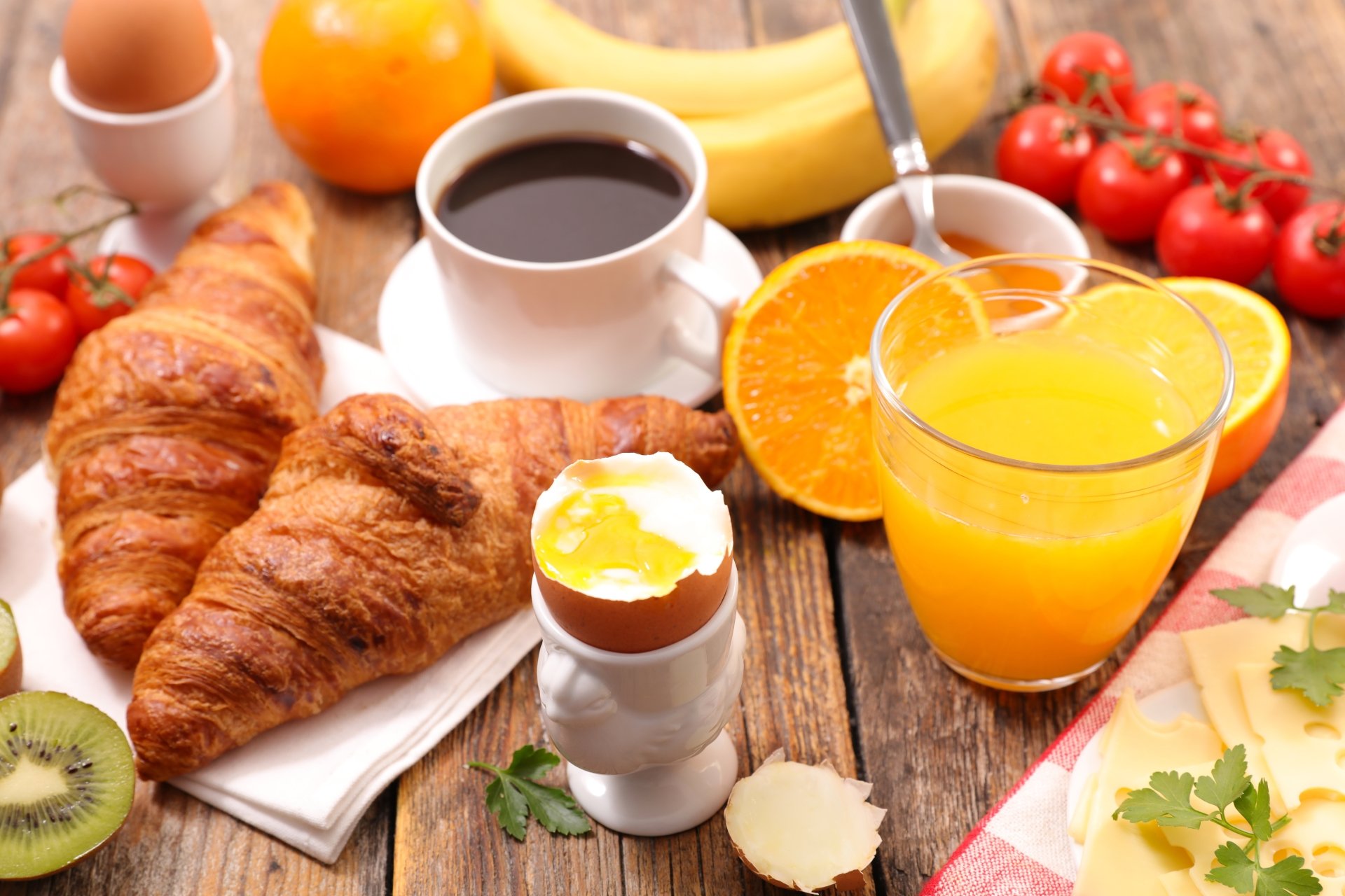 8K Ultra HD still life of a breakfast featuring croissants, a cup of coffee, fresh orange juice, and assorted fruits on a rustic wooden table.
