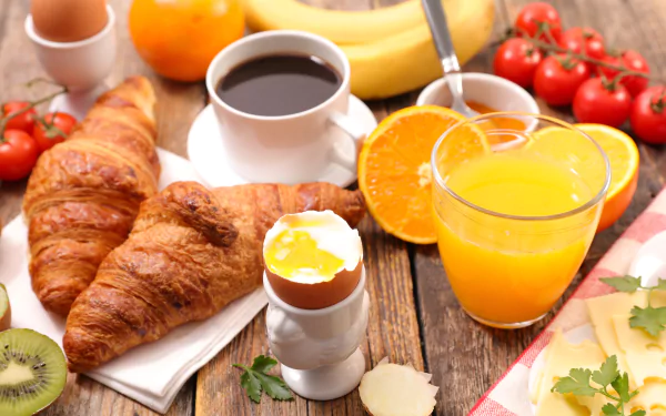 8K Ultra HD still life of a breakfast featuring croissants, a cup of coffee, fresh orange juice, and assorted fruits on a rustic wooden table.