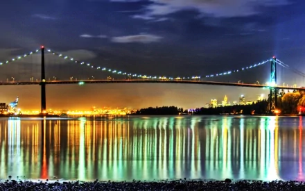 Night view of the illuminated Lions Gate Bridge in Vancouver, Canada, with city lights reflecting on the calm water below.