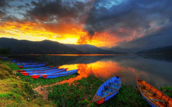 HD desktop wallpaper of vibrant sunset over calm water with colorful canoes lined along the shore, under a dramatic sky.