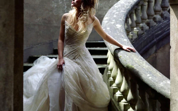 Keira Knightley stands elegantly on a staircase, wearing a stunning gown that cascades around her, captured in a striking HD wallpaper background.