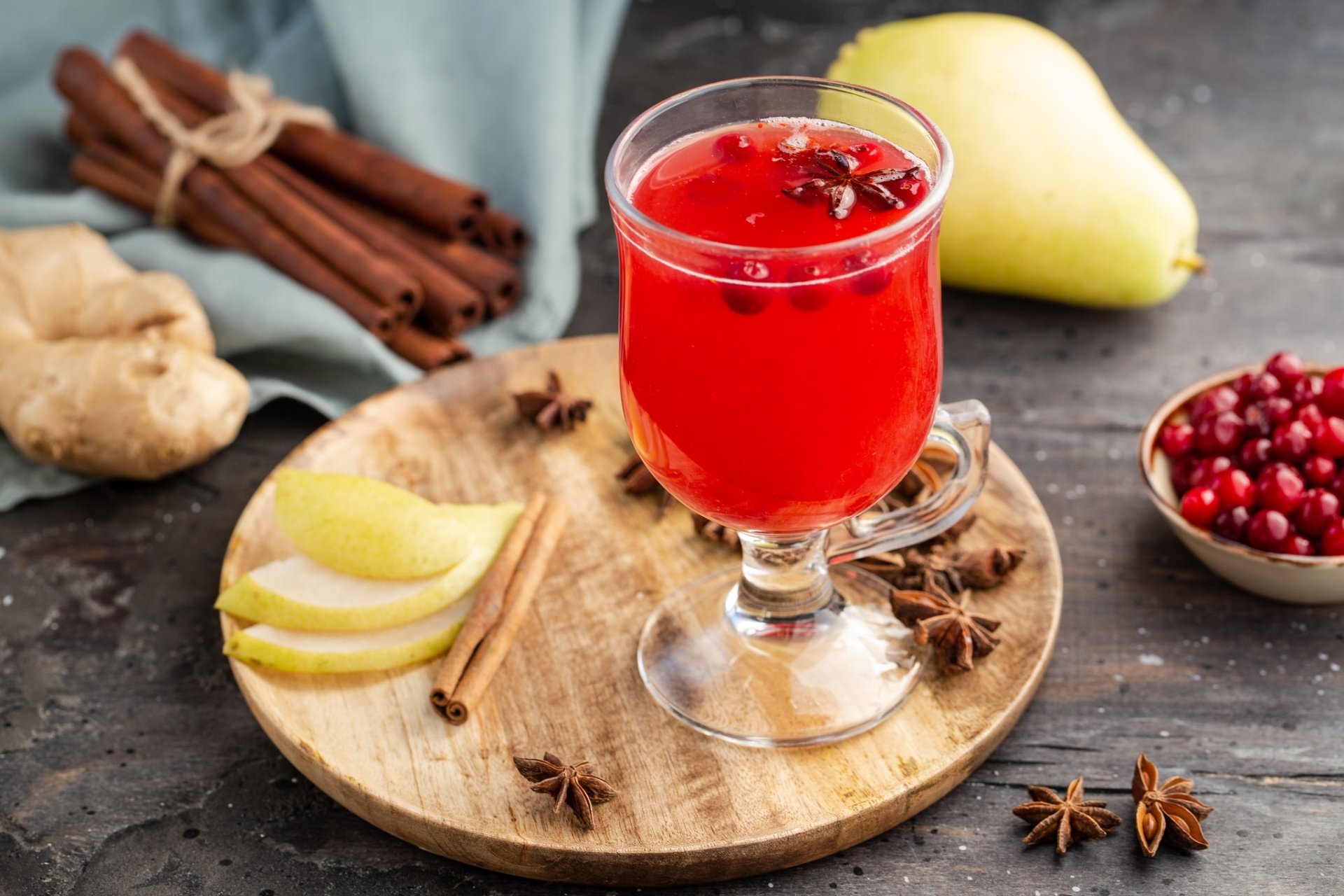 HD still life desktop wallpaper featuring a red spiced drink with star anise, cinnamon sticks, sliced pear, ginger, and cranberries arranged on a wooden board.