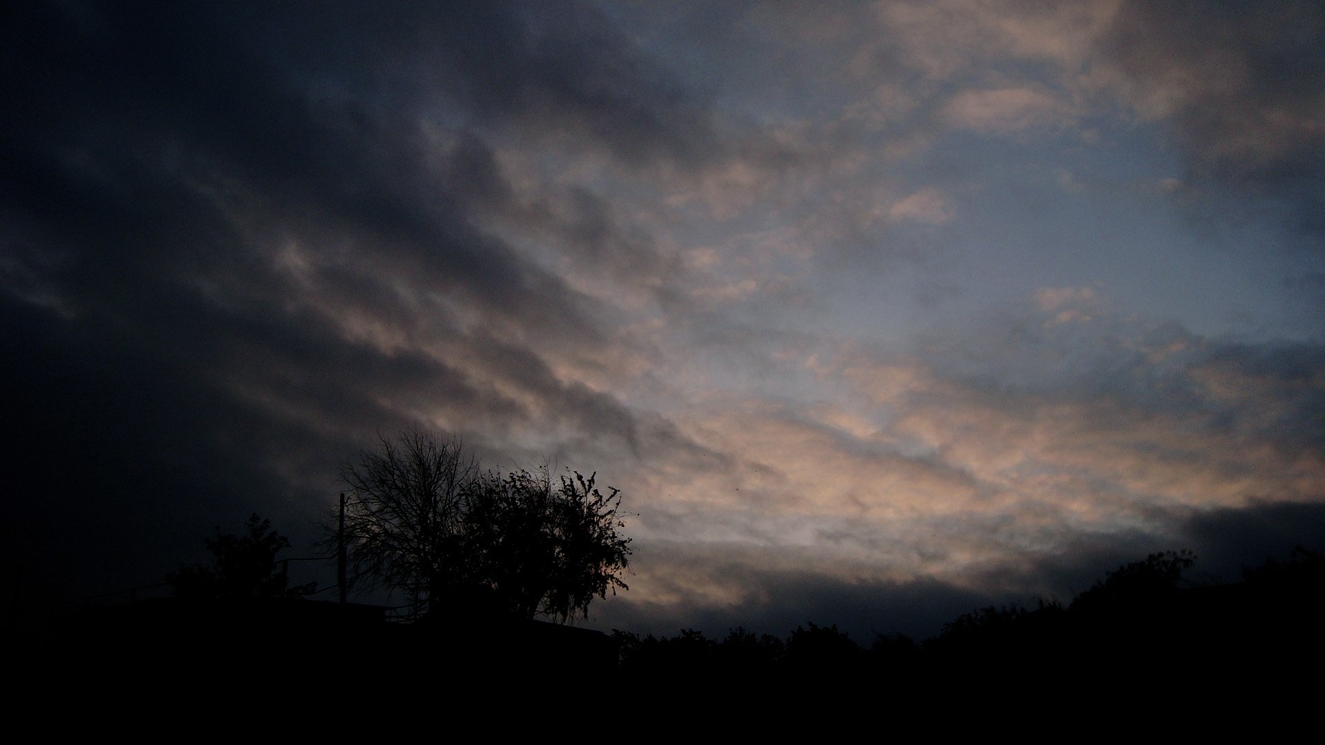 HD PC desktop wallpaper of nature: moody twilight sky with layered clouds sweeping over silhouetted trees and horizon.