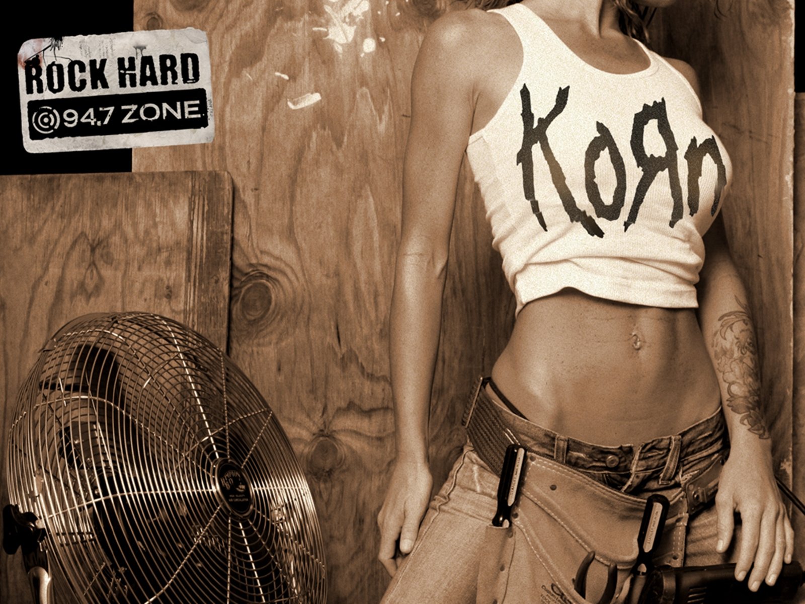 HD PC desktop wallpaper featuring a person wearing a cropped Korn band tank top, with a vintage fan and Rock Hard @947 Zone sticker in the background, emphasizing music and Korn.