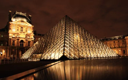 A stunning view of the Louvre in Paris at night, featuring the iconic glass pyramid illuminated against a dramatic sky, showcasing man-made beauty in France.