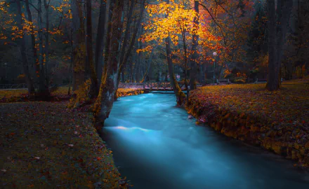 HD desktop wallpaper of a serene river flowing under a bridge in a park, surrounded by trees with vibrant fall foliage.