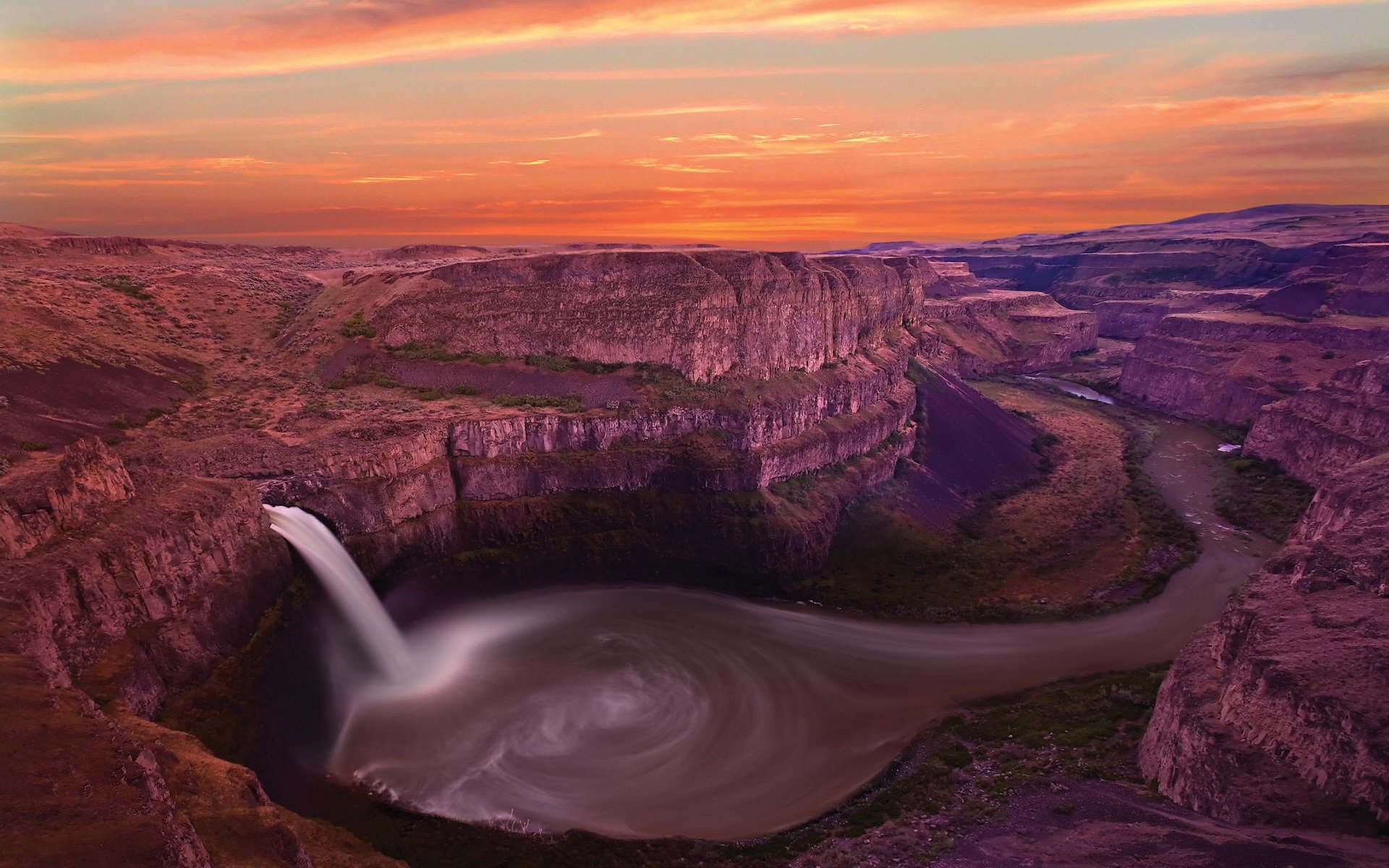 HD PC desktop wallpaper showcasing Palouse Falls cascading into a swirling pool at sunset, set against rugged canyon cliffs under a colorful sky.