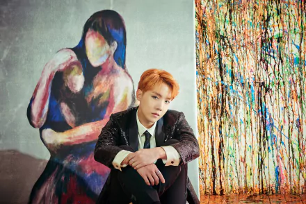 HD desktop wallpaper featuring K-pop singer J-Hope from BTS sitting in front of vibrant, abstract artwork.