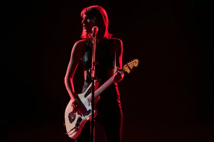 Taylor Swift performing with an electric guitar on stage, captured in a dramatic red and black 4K Ultra HD music wallpaper.