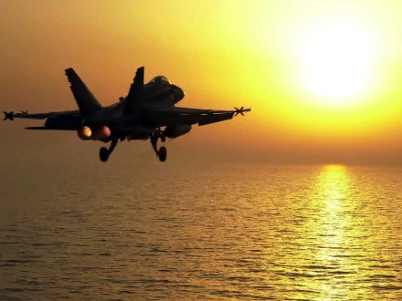 A Boeing F/A-18E/F Super Hornet flies over the ocean at sunset, showcasing its powerful design against a vibrant sky. This stunning image serves as an HD PC desktop wallpaper.