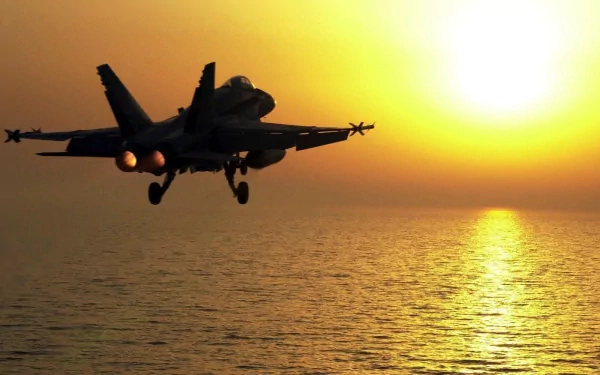 A Boeing F/A-18E/F Super Hornet flies over the ocean at sunset, showcasing its powerful design against a vibrant sky. This stunning image serves as an HD PC desktop wallpaper.