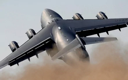 A Boeing C-17 Globemaster III takes off, kicking up a cloud of dust as its powerful engines roar. This high-definition image serves as a striking military-themed desktop wallpaper.