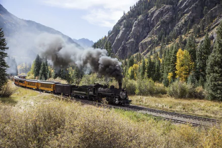 HD desktop wallpaper featuring a vintage black locomotive train moving through a scenic mountain valley surrounded by autumn trees and rugged cliffs.