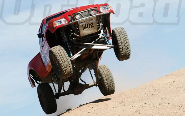 A dynamic HD image of a red Ford Ranger off-road vehicle leaping over a sandy dune, showcasing its rugged design and power in action.