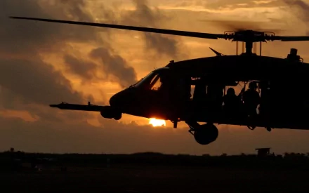 Silhouette of a Sikorsky HH-60 Pave Hawk military helicopter flying at sunset, captured in an HD PC desktop wallpaper and background.