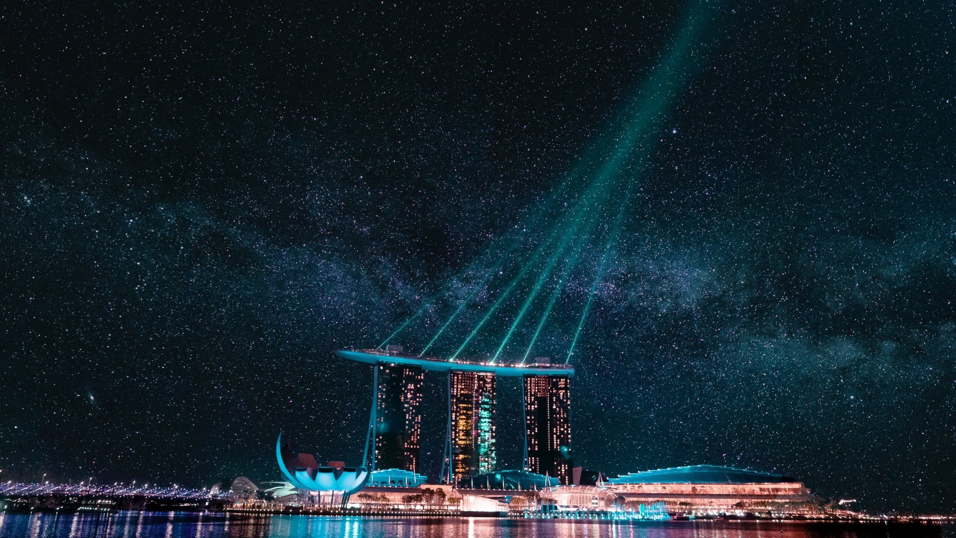 Night view of Marina Bay Sands in Singapore with a starry sky and vibrant light beams over the marina, captured in 4K Ultra HD.