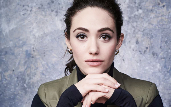 HD desktop wallpaper of a brunette American actress and celebrity with brown eyes, poised against a textured gray background, hands clasped under her chin and looking directly at the camera.