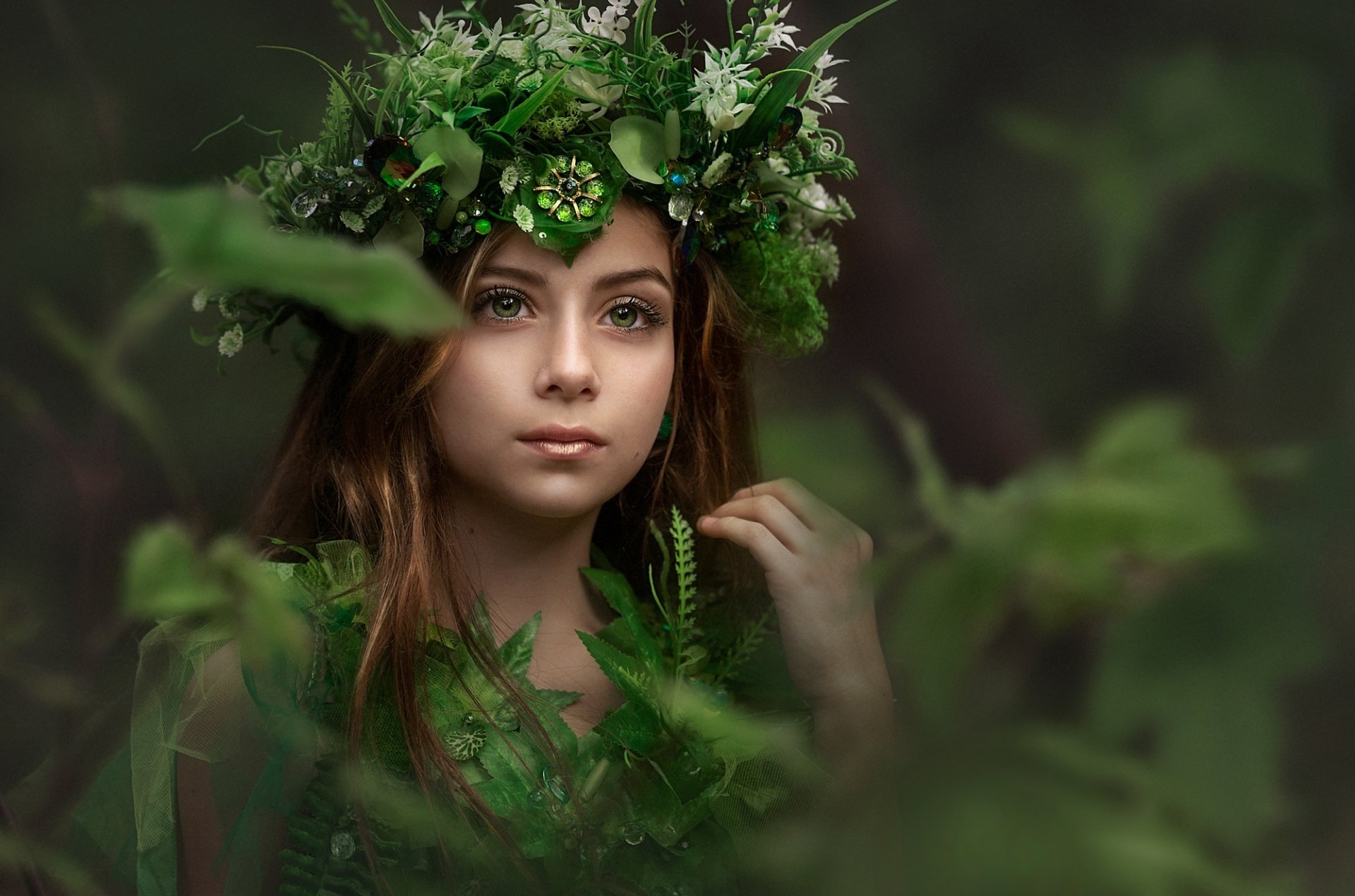 A serene image of a woman adorned with a green floral crown, surrounded by lush foliage. The image is in high definition, making it a stunning wallpaper and background option for desktops.