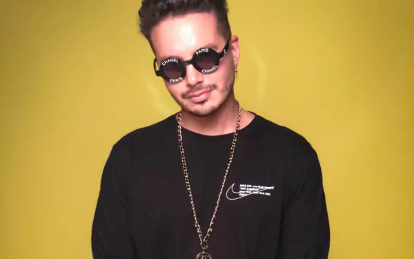 HD wallpaper featuring J Balvin, wearing sunglasses and a black shirt, against a vibrant yellow background, exuding a cool, stylish vibe in the realm of music.