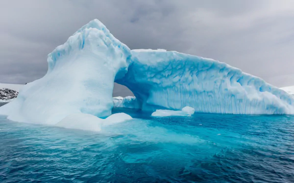 HD PC desktop wallpaper featuring a striking iceberg formation floating in calm, icy blue waters under a cloudy sky, showcasing the beauty of nature.