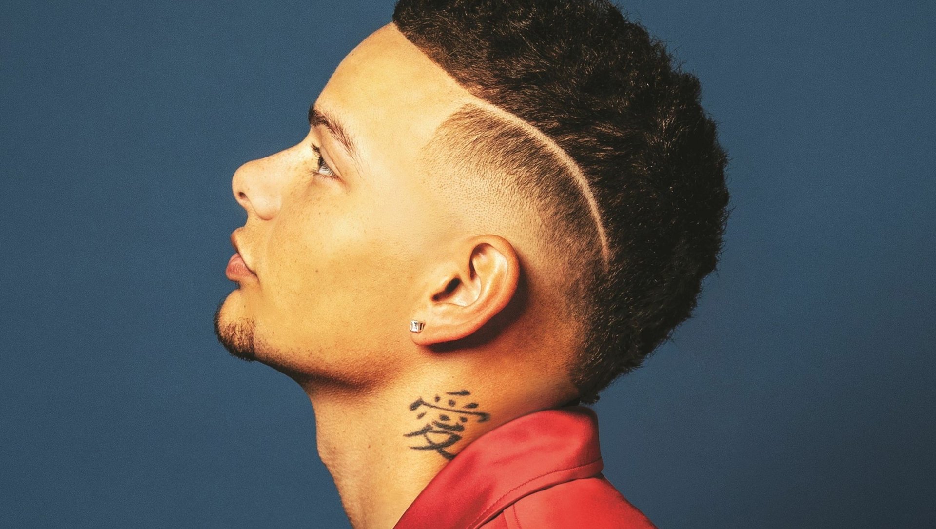 HD desktop wallpaper featuring a profile view of a man with a high fade haircut and a neck tattoo against a blue background.