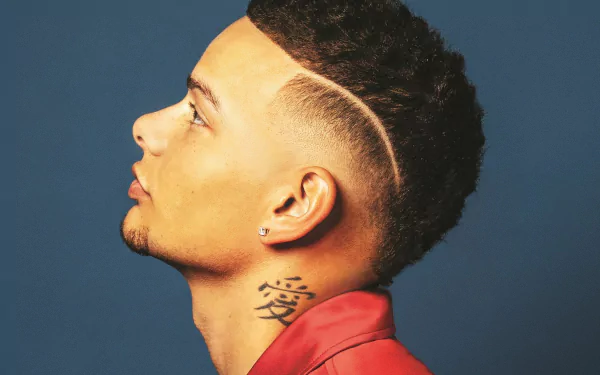 HD desktop wallpaper featuring a profile view of a man with a high fade haircut and a neck tattoo against a blue background.