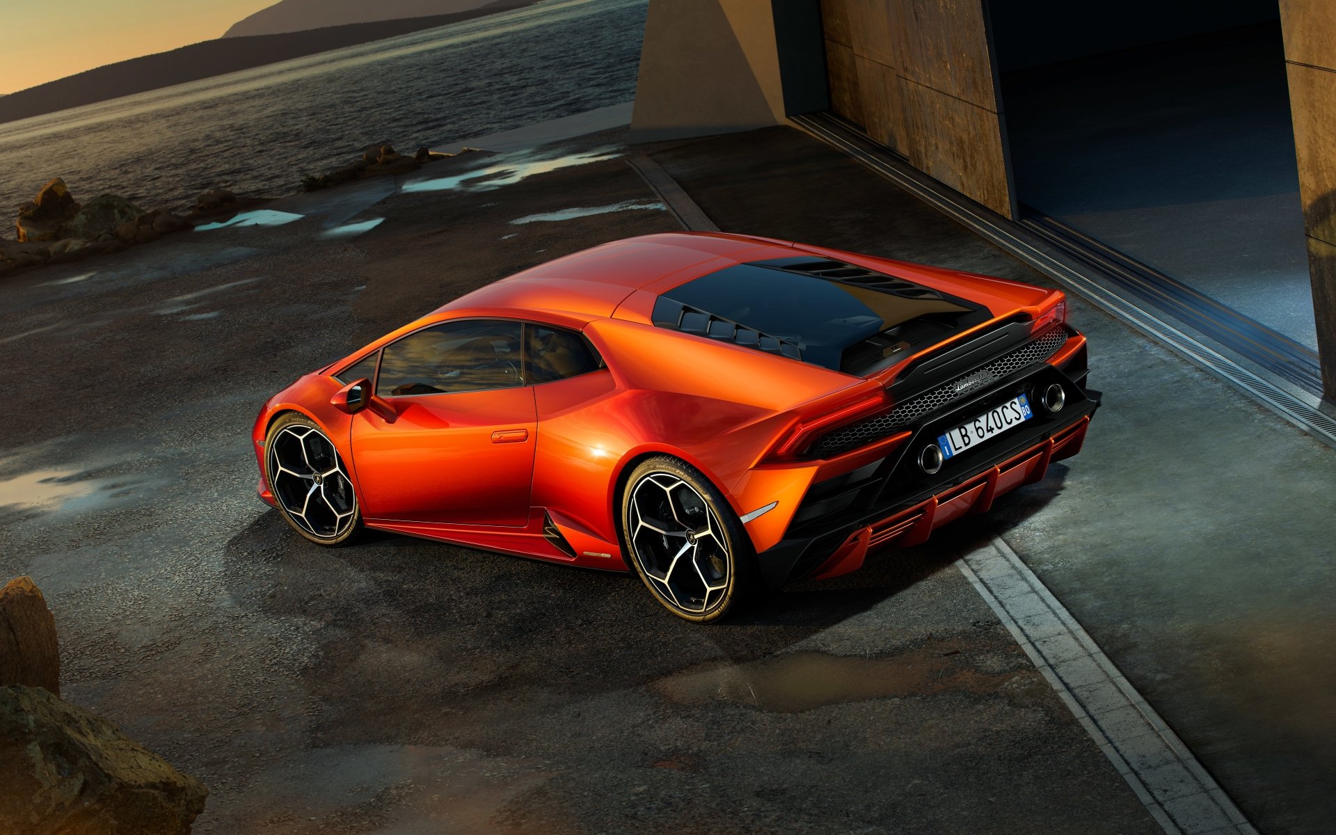 8K Ultra HD PC desktop wallpaper of an orange Lamborghini Huracan Evo supercar parked on a coastal concrete driveway by a modern garage, dramatic lighting and high-detail background.