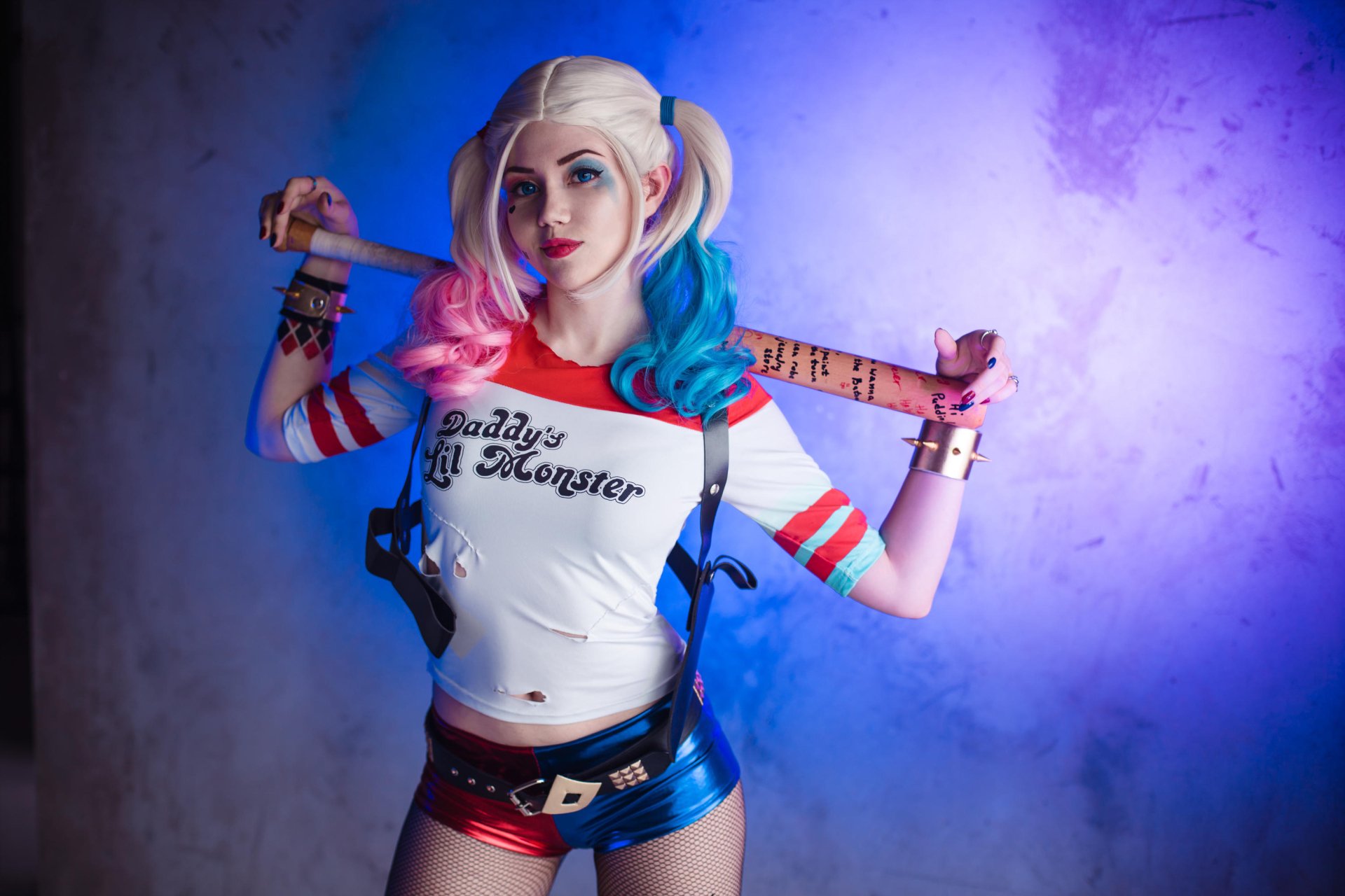 HD desktop wallpaper of a blonde woman with twintails and blue eyes, dressed in Harley Quinn cosplay, wearing shorts and holding a baseball bat over her shoulders.