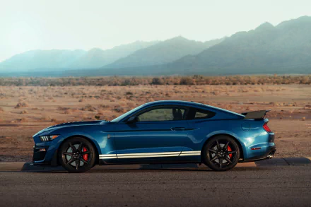 A blue Ford Mustang Shelby GT500 muscle car parked on a desert road with mountains in the background, captured in 8K Ultra HD for a PC desktop wallpaper.