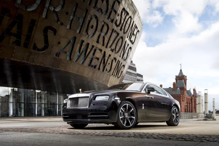 Black Rolls-Royce Wraith parked before a curved metallic modern building and a nearby red-brick tower under a partly cloudy sky — 5K Ultra HD PC desktop wallpaper.