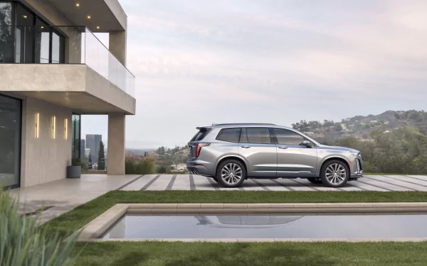 Silver Cadillac XT6 SUV parked beside a modern house and pool with rolling hills, 5K Ultra HD PC desktop wallpaper background.