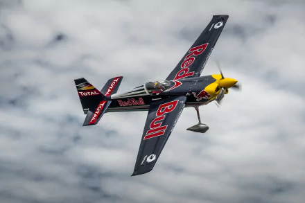 Red Bull Air Race airplane with Red Bull livery banking over a cloudy sky — 2K Quad HD PC desktop wallpaper/background