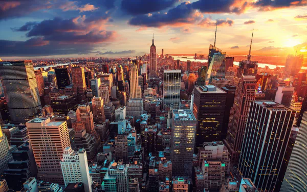 A stunning HD desktop wallpaper of New York City, showcasing a sprawling cityscape filled with towering skyscrapers under a dramatic sunset sky in the USA.
