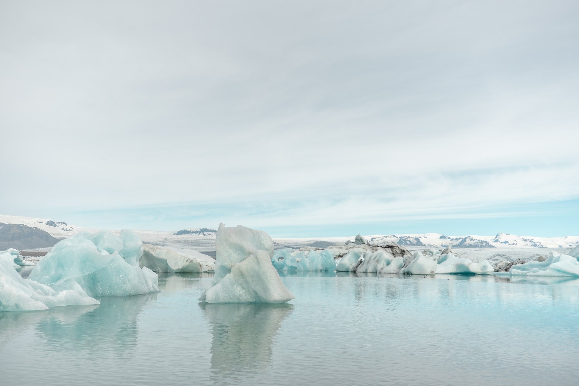 4K Ultra HD PC desktop wallpaper of a serene lagoon dotted with icebergs under a soft, cloudy sky, showcasing the beauty of nature’s icy landscape.