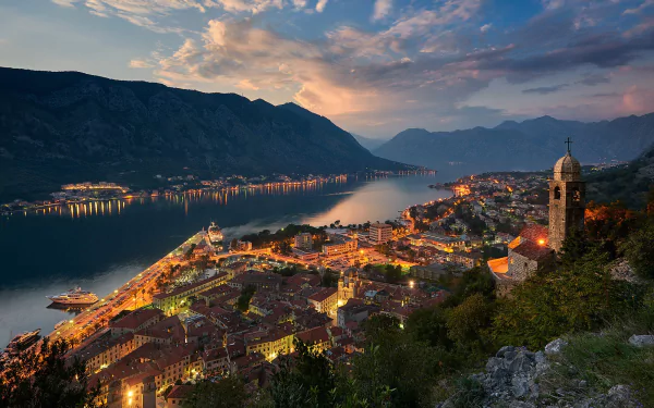 HD desktop wallpaper of a Montenegro town at dusk, featuring a river winding through the man-made landscape with mountains in the background under a colorful sky.