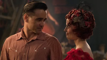 HD desktop wallpaper: still from the movie Dumbo (2019) showing two costumed characters — a man in a checkered shirt and a woman in a red beaded dress and ornate headpiece sharing a warm glance.