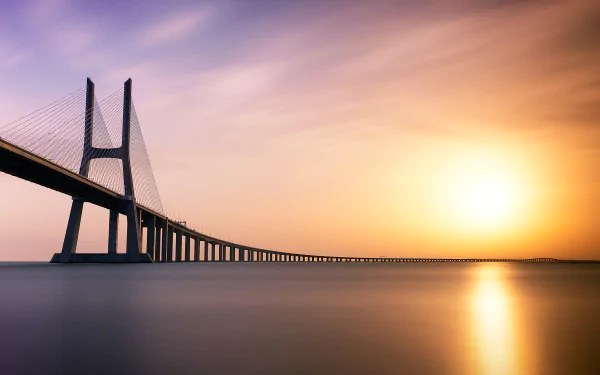 Vasco da Gama Bridge in Portugal stretches over calm water at sunset, captured in a 4K Ultra HD desktop wallpaper and background.