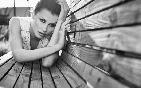Black and white HD desktop wallpaper featuring celebrity Bridget Moynahan lying on a wooden surface, with an intense and captivating gaze.