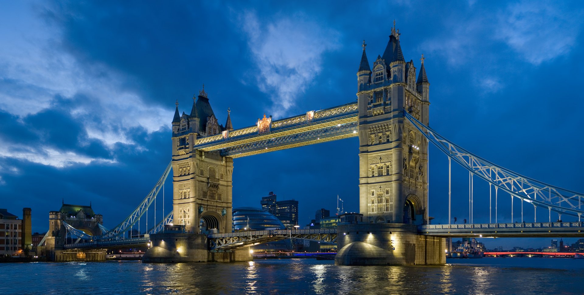 HD desktop wallpaper showcasing the illuminated Tower Bridge, a man-made architectural landmark, against a dramatic evening sky over the River Thames.