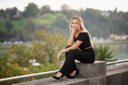 A blonde woman with long hair and a warm smile sits wearing black high heels and an off-shoulder outfit, captured in sharp 4K Ultra HD with a soft depth of field background.