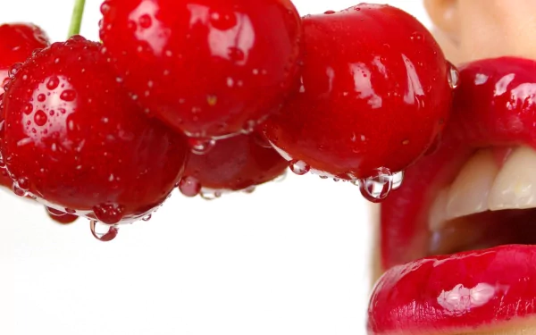 A close-up of a mouth holding a cluster of glistening cherries, showcasing vibrant colors and textures, serving as a striking HD desktop wallpaper and background.